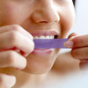 Uśmiechnięta kobieta w szlafroku trzyma fioletowe serum korygujące kolor zębów Diamond Smile.